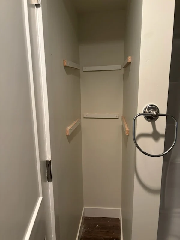 Finished white shelving installed on the back and side walls of a narrow closet.