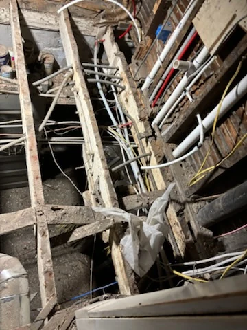 Exposed floor joists beside open wall framing, with existing pipes and wiring visible.