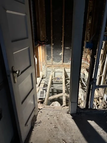 View through a doorway into an interior with floorboards removed and joists exposed.