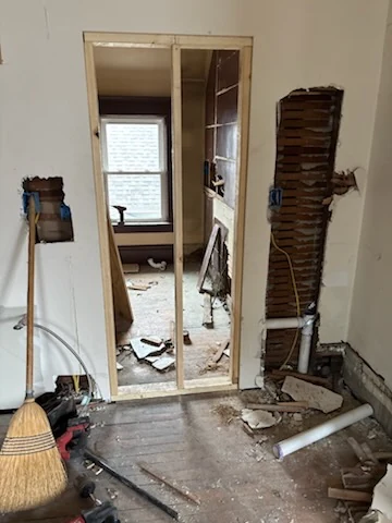 Interior doorway with wall surfaces removed, exposed lath, and demolition debris on the floor.