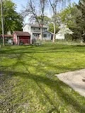 Mowed backyard lawn beside a concrete walkway and trees.