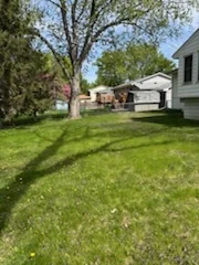 Mowed backyard lawn between homes and mature trees.