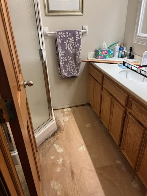Bathroom floor with tile removed beside a wood vanity and shower.