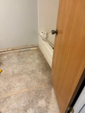 Cleared bathroom floor with the toilet and tile removed beside a bathtub.