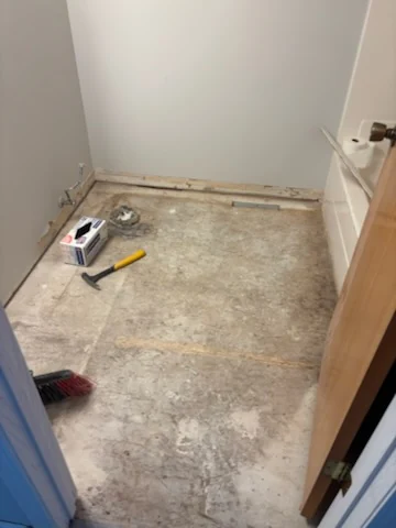 Bathroom floor cleared of tile with hand tools near the wall.