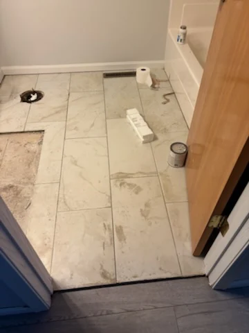 Bathroom floor covered with fitted light-colored panels after tile removal.