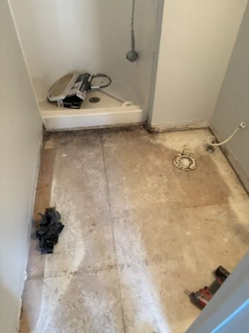 Bathroom floor after tile removal between a shower and toilet connection.