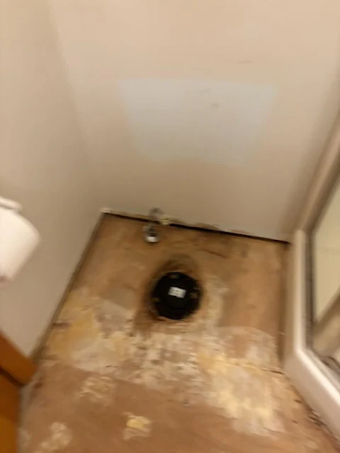 Small bathroom floor after tile removal around an exposed toilet connection.