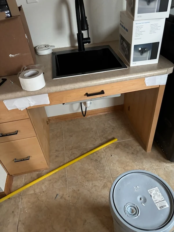 Bathroom vanity area during floor work with tools, a sink, and exposed flooring visible.